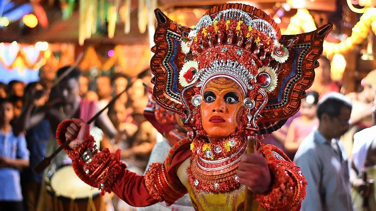 A performer in traditional Theyyam costume with vibrant face paint and a large headgear