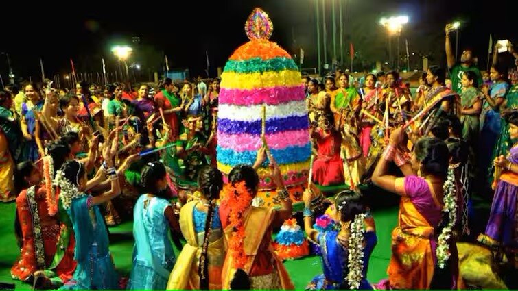 Women performing the Bathakamma dance, gracefully spinning and clapping around a beautifully decorated flower structure, symbolizing the goddess Bathakamma.