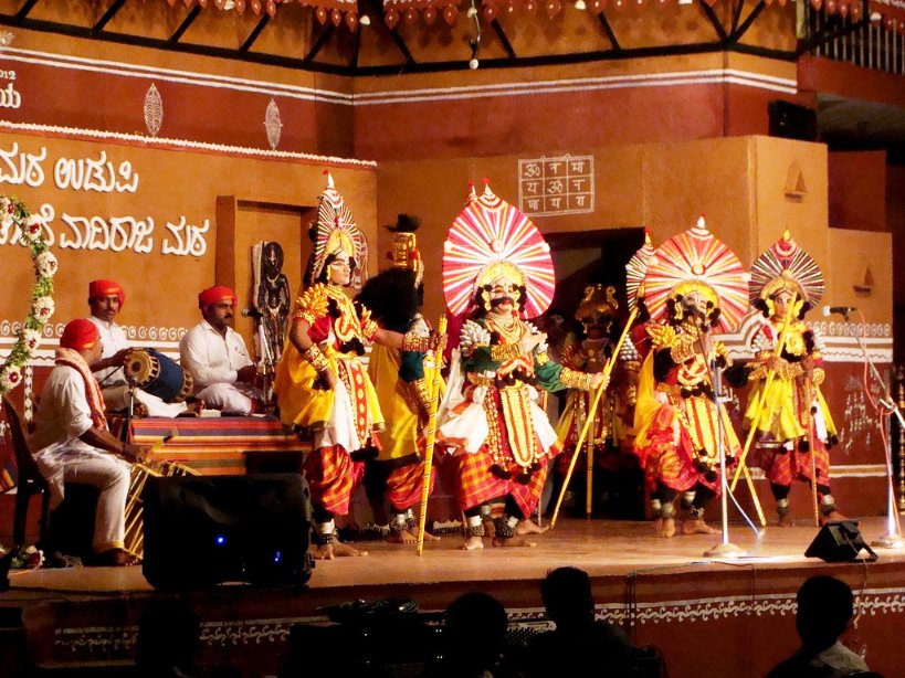 Yakshagana performance on an open stage with vibrant costumes, dramatic facial makeup