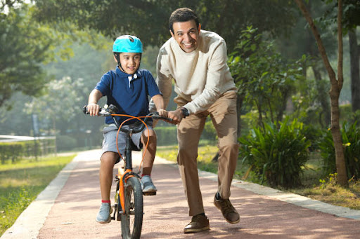 Boy learning bicycle with the assistance of father at the park.