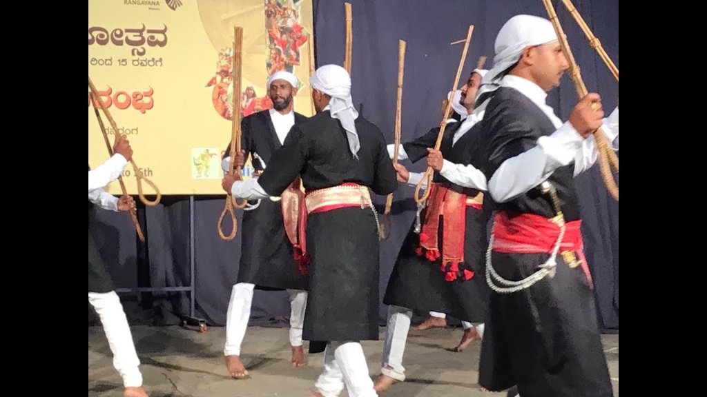 Performers of Huttari dance, dressed in traditional attire, energetically dancing to celebrate the harvest festival in Karnataka, showcasing synchronized movements, vibrant costumes, and rhythmic footwork