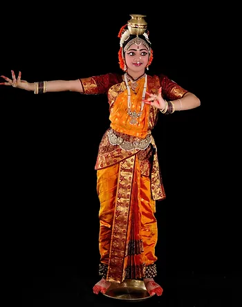 A graceful Kuchipudi dancer performing traditional movements in a bright and elaborate costume. The dancer is posed mid-movement with her hand gestures