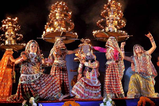 A Charkula dancer balancing a multi-tiered wooden pyramid adorned with oil lamps on her head.