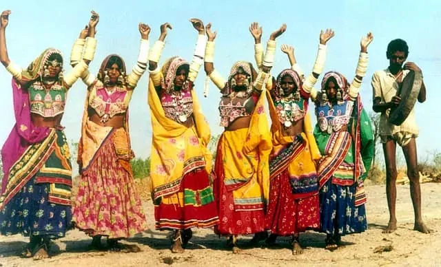 A vibrant image of women performing the Lambadi dance in colorful attire, their movements energetic and synchronized. The dancers are spinning and clapping in a circle during a lively festival celebration.