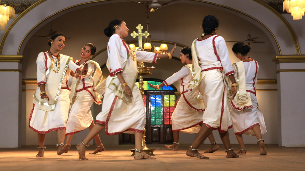 A group of 12 dancers in traditional white clothes, performing Margamkali in a circular arrangement around an oil lamp