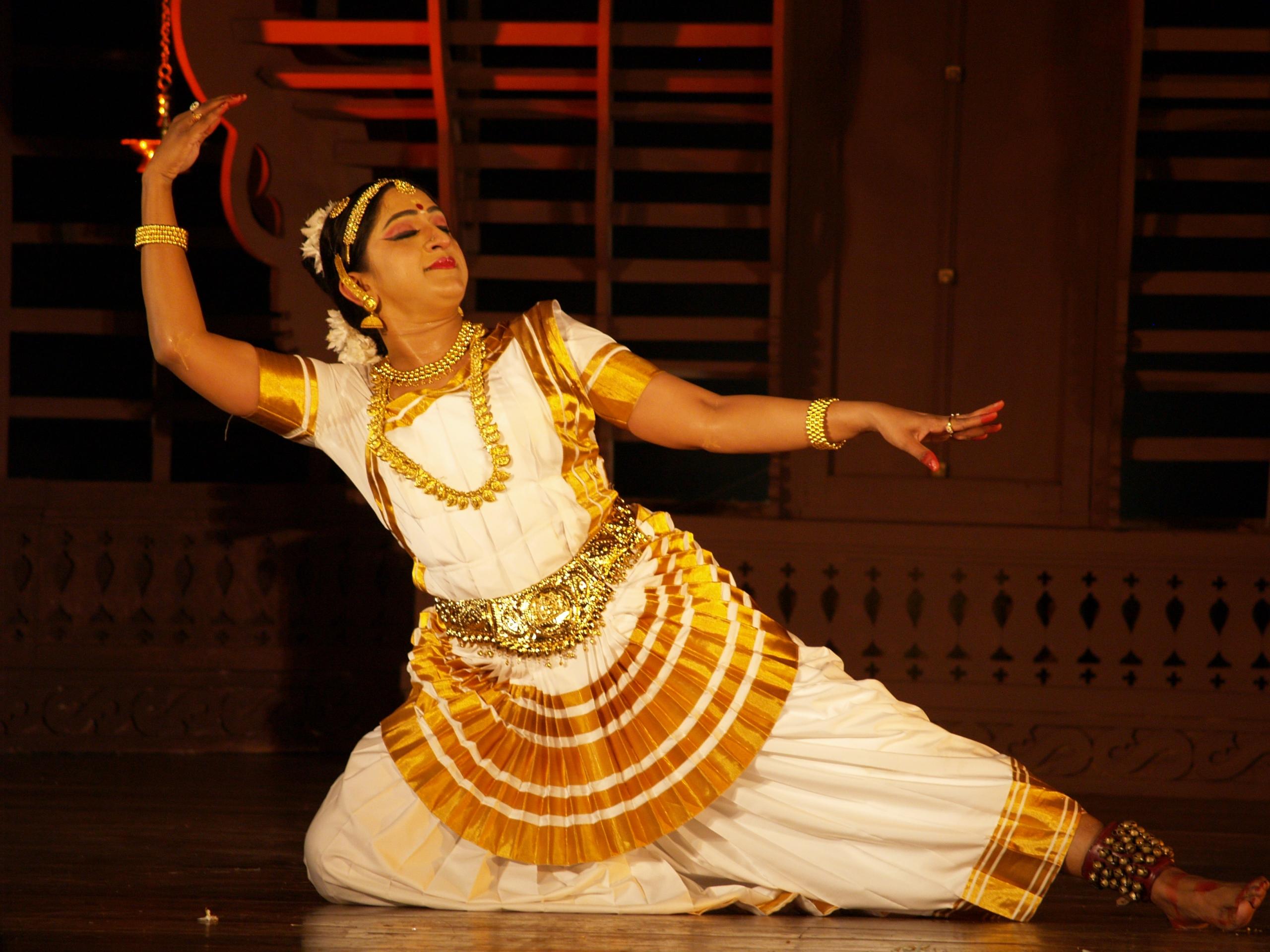 A female dancer performing Mohiniyattam, wearing a traditional white and gold saree with jasmine flowers